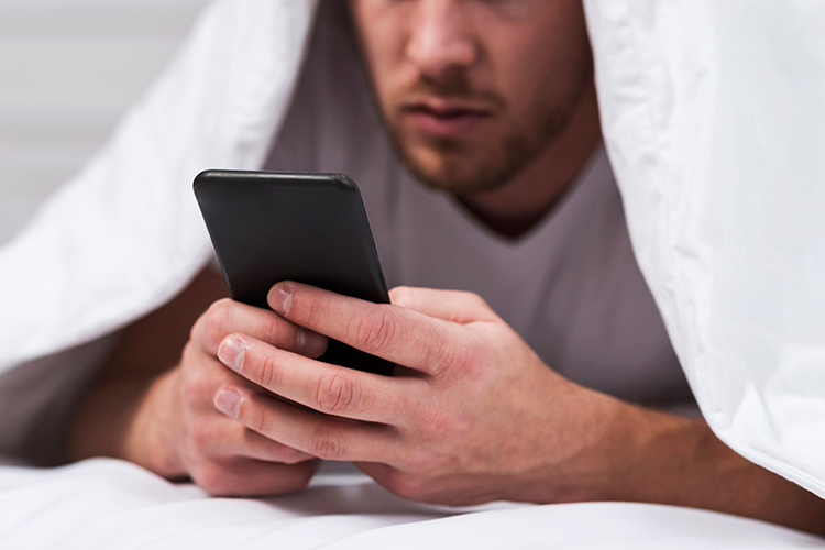 Bild zeigt Mann im Bett mit Handy