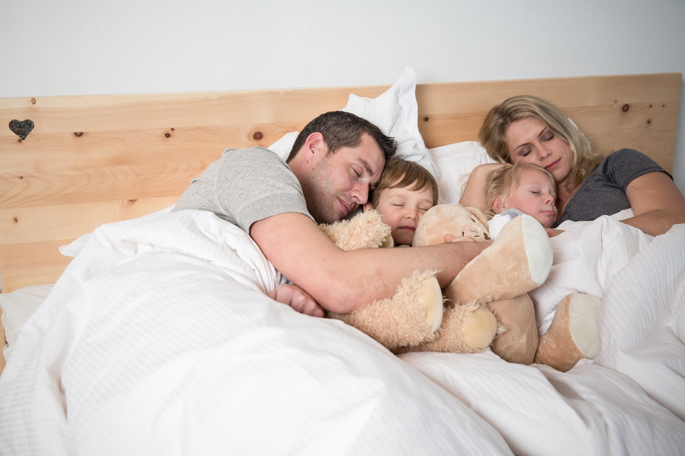 Frau im Bett hält in einer Hand Kaffee und in der anderen das Handy