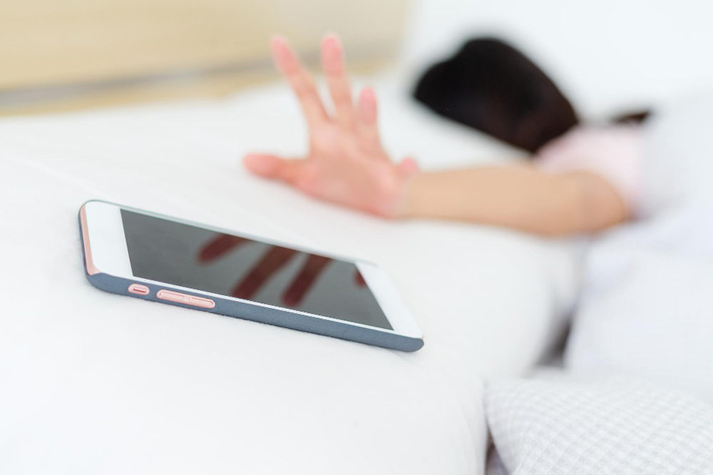 Frau im Bett greift nach dem Handy