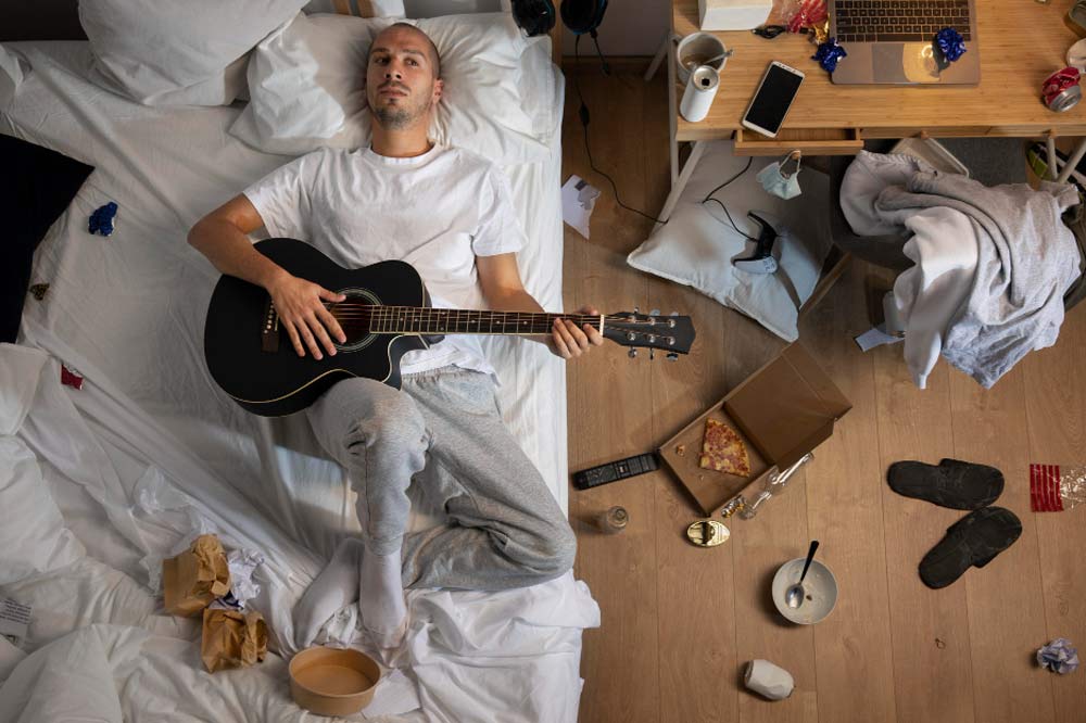 Mann liegt mit Gitarre am Bett